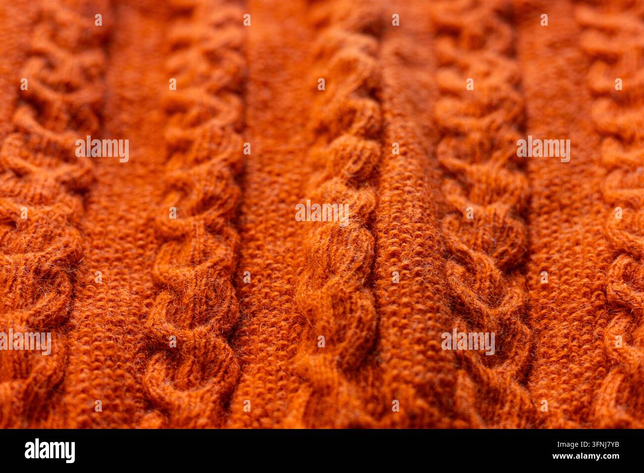 Primo piano di tessuto a maglia di maglione arancione con motivi intrecciati in rilievo e fibre di lana morbide, che creano uno sfondo tessile caldo ispirato all'autunno Foto Stock