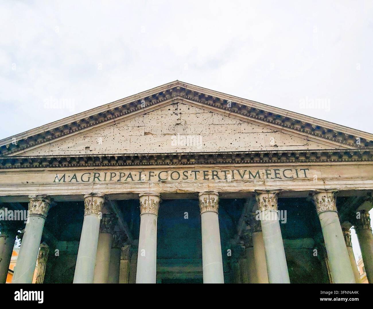 Pedimento del portico romano antico e iscrizione latina sul tempio storico del Pantheon a Roma, Italia, sotto un cielo di luce diafana ma coperto. Foto Stock