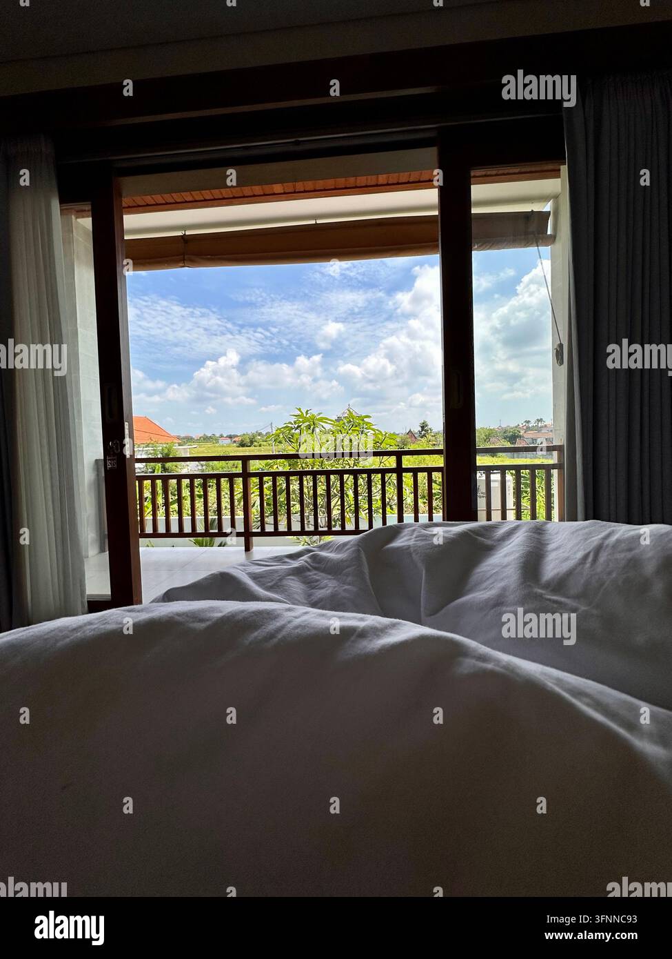 La biancheria da letto bianca sgualcita si affaccia su un balcone frondoso attraverso porte di vetro alla luce del giorno. - Immagine stock catturata con smartphone
