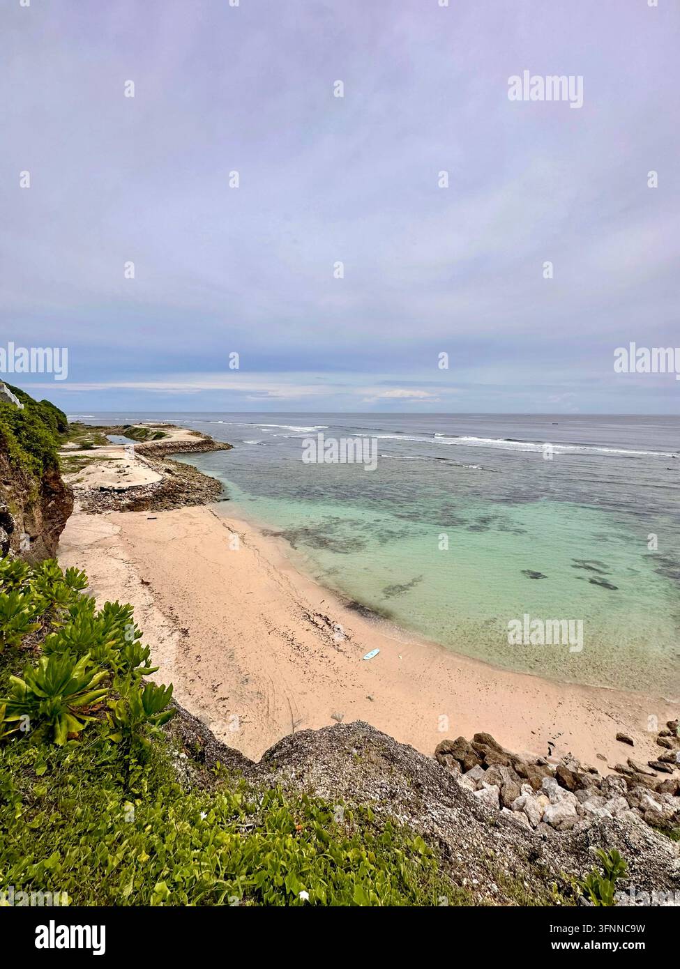 Acque turchesi incontrano una spiaggia sabbiosa ai piedi delle scogliere costiere sotto una luce soffusa e nuvolosa. - Immagine stock catturata con smartphone