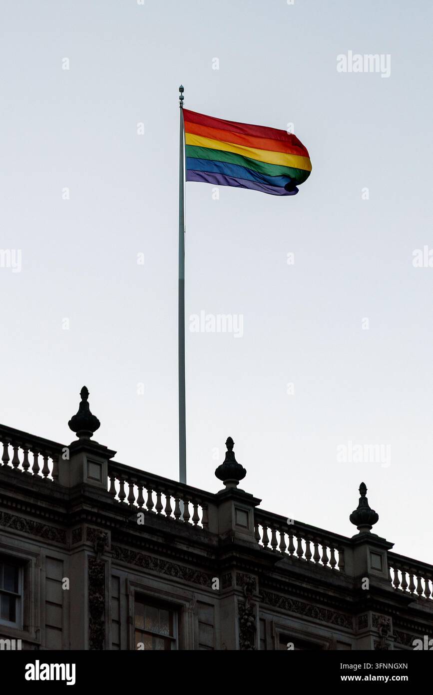 Scatto verticale ad angolazione bassa di una vivace bandiera arcobaleno pride che sventola su un alto asta sopra una balaustra in pietra classica ornata. Il colorato Foto Stock