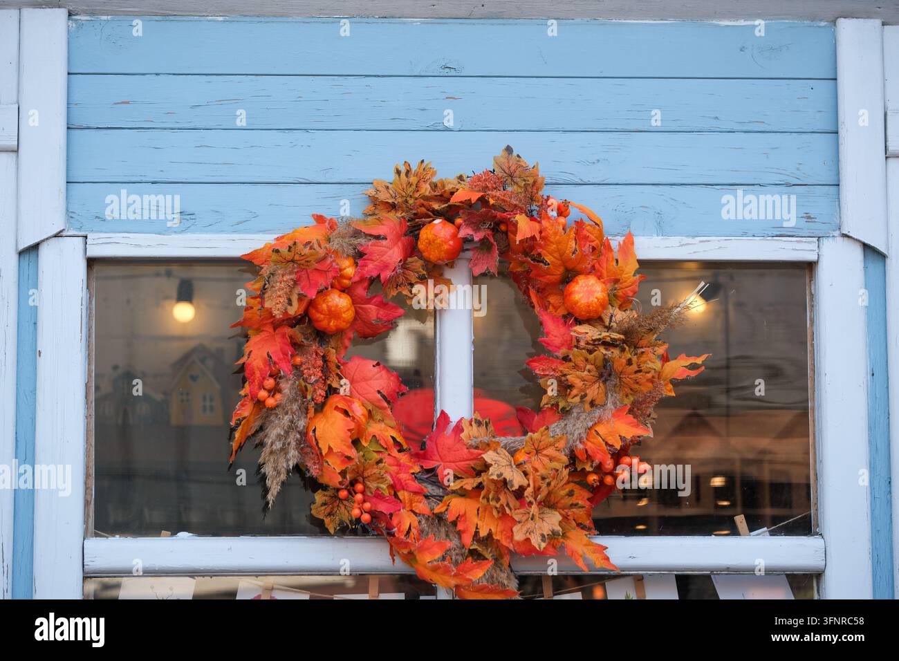 Una colorata ghirlanda autunnale decora una finestra di legno blu sopra una vetrina del negozio. Foto Stock