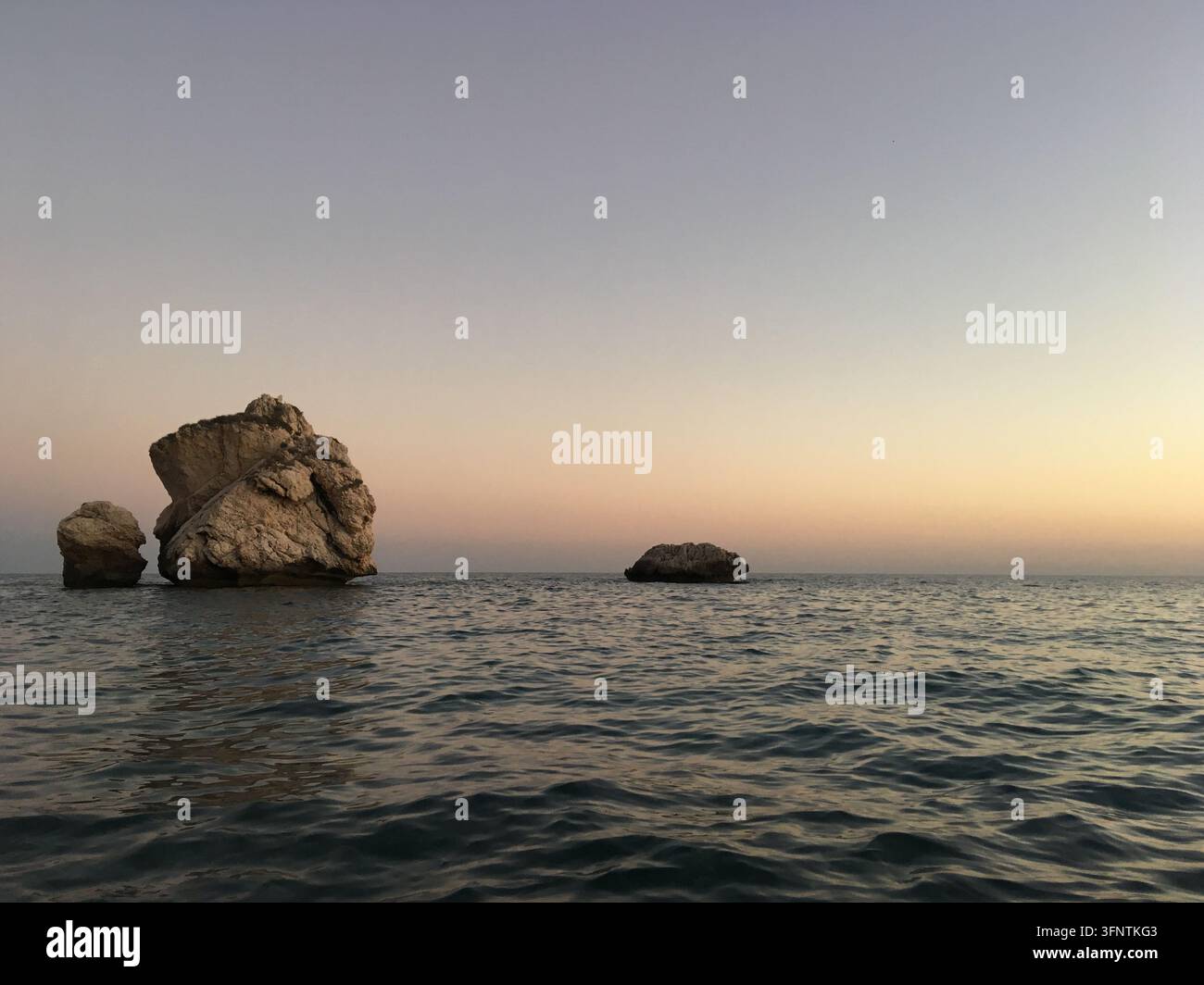 Vista del tramonto sul Mar Mediterraneo vicino a Paphos, Cipro. Due promontori rocciosi si ergono dall'acqua, uno dei quali è significativamente più grande. Il cielo di Foto Stock
