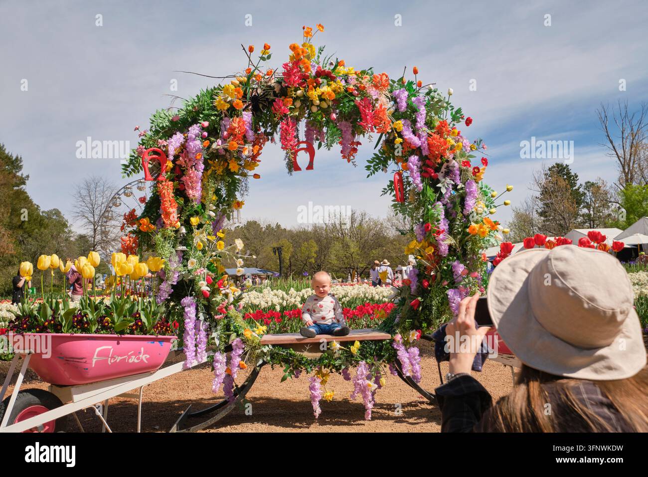 Un bambino che posa per un ritratto sotto un bouquet gigante, una mostra di ghirlande. Alla Floriade, la festa annuale dei fiori e dei tulipani a Canberra, in Australia. Foto Stock