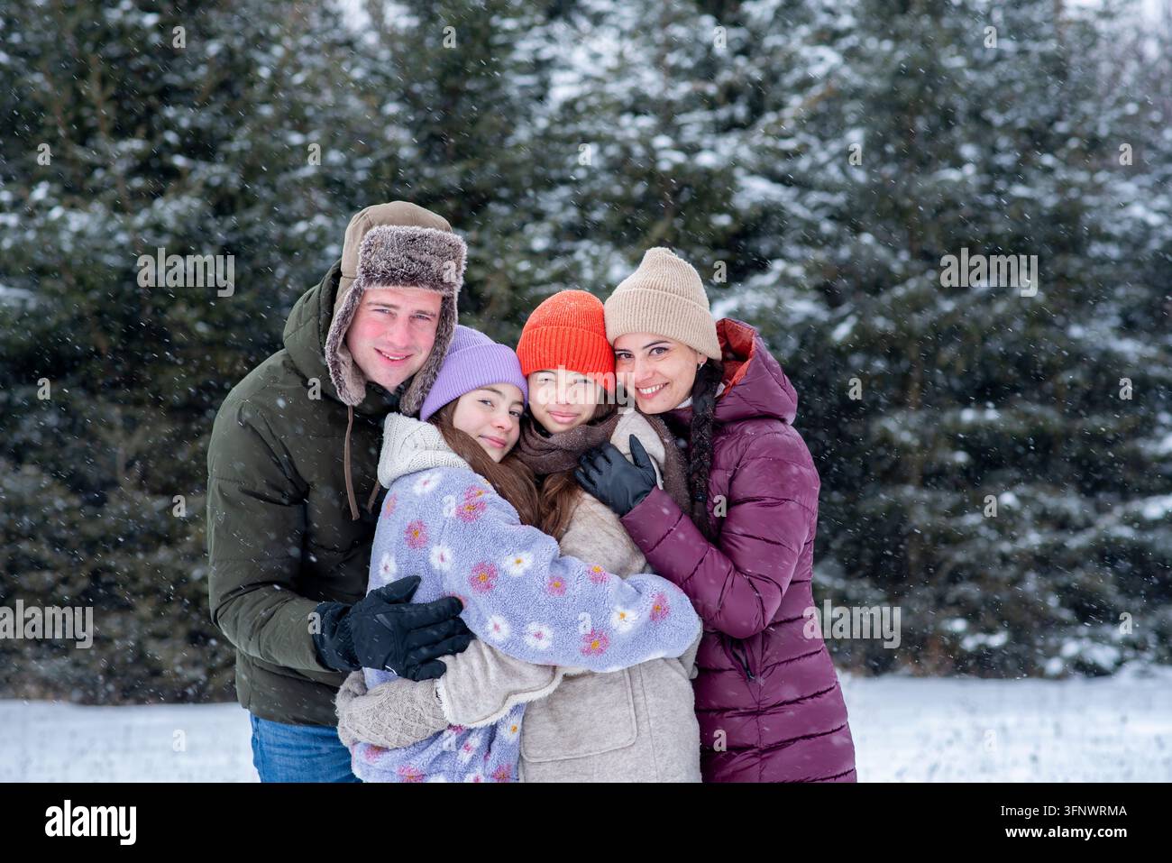 Famiglia felice insieme durante le nevicate nella foresta invernale. Foto Stock