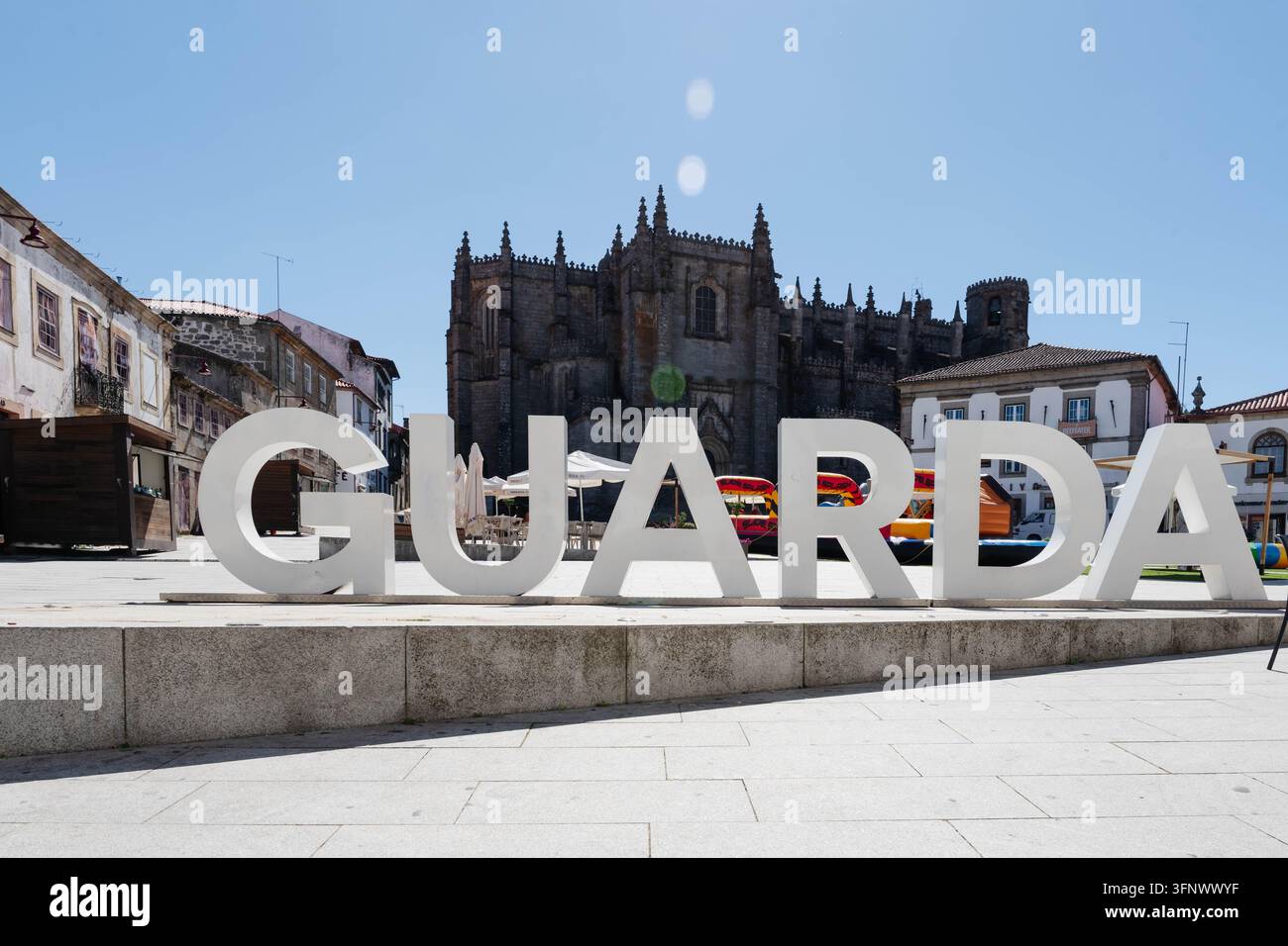 Guarda, Portogallo - 12 settembre 2026 Grandi lettere bianche con il nome della città si trovano su una piazza davanti alla cattedrale gotica con ombrelloni e un gonfiabile Foto Stock