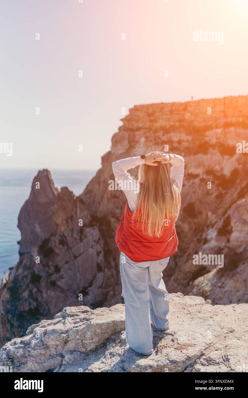 Donna sulla scogliera sull'oceano in piedi su un precipizio roccioso che si affaccia sul mare blu al tramonto per un senso di libertà Foto Stock