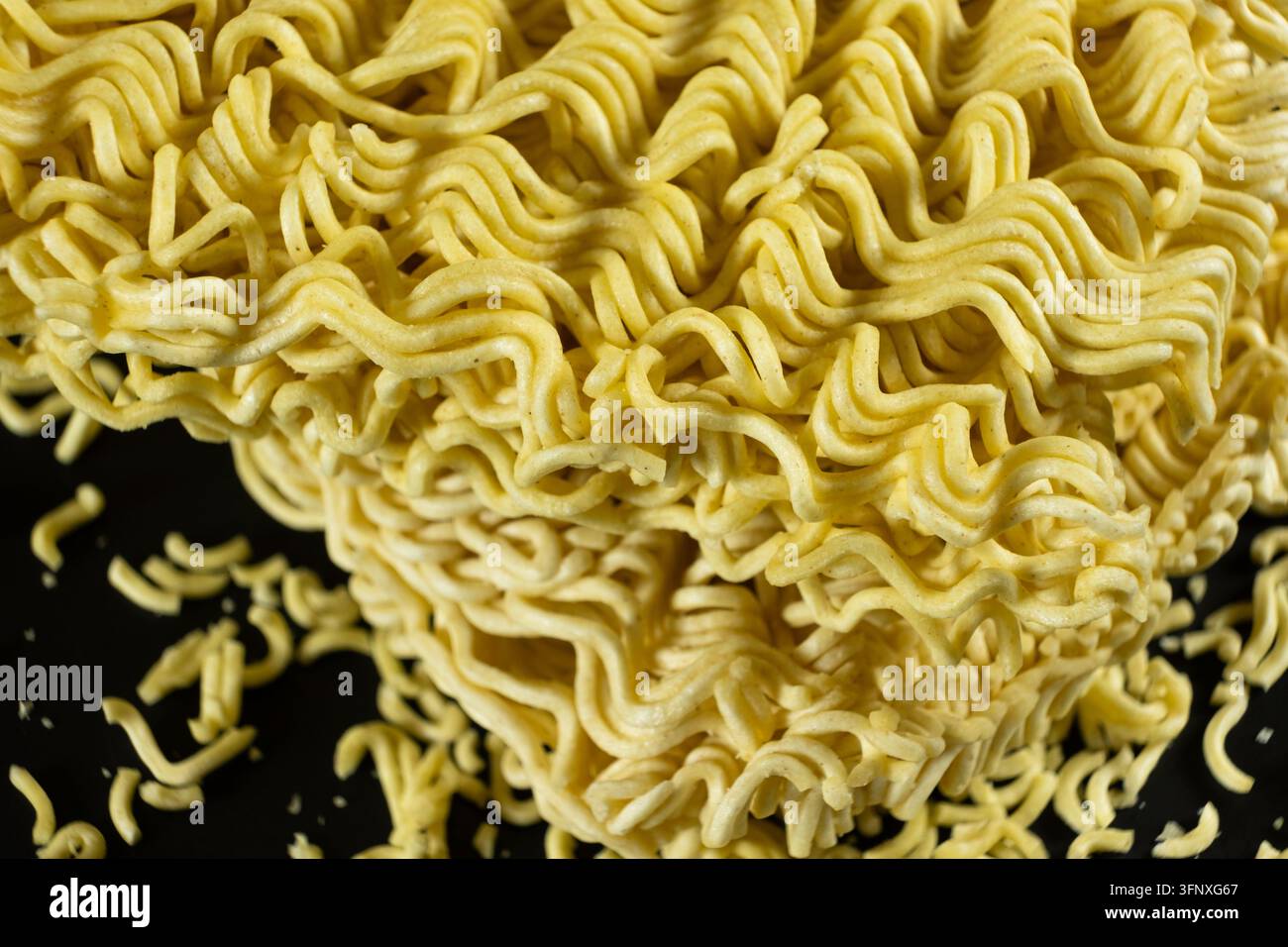 Nudli istantanei asciutti ondulati con piccoli pezzi su sfondo scuro. Foto Stock