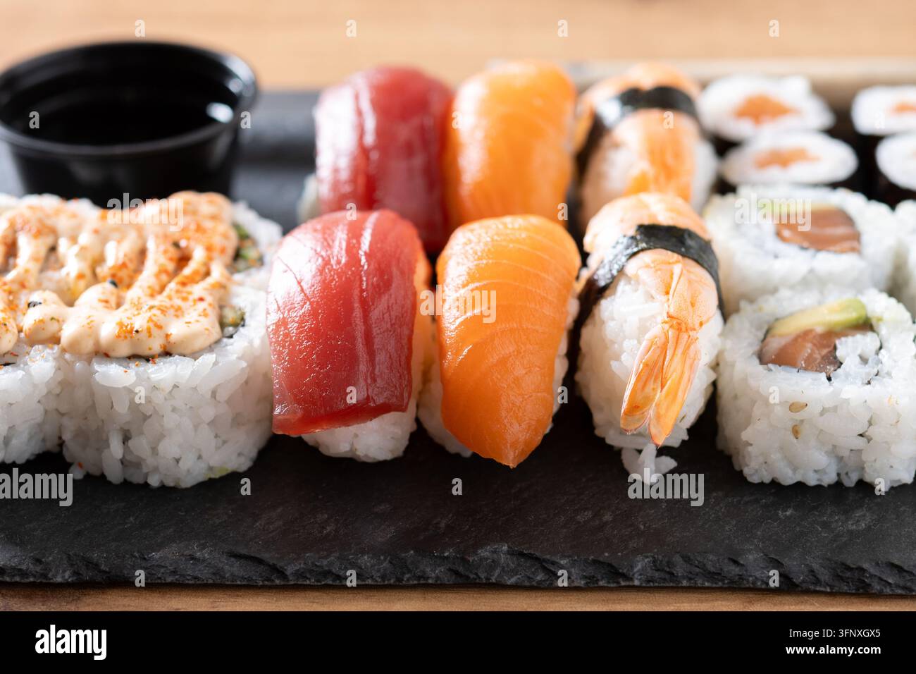 Prima piano di un vassoio di sushi assortito con nigiri di salmone, tonno e gamberetti con rotoli di maki, servito su una tavola di ardesia scura. Concetto di cibo giapponese. Foto Stock