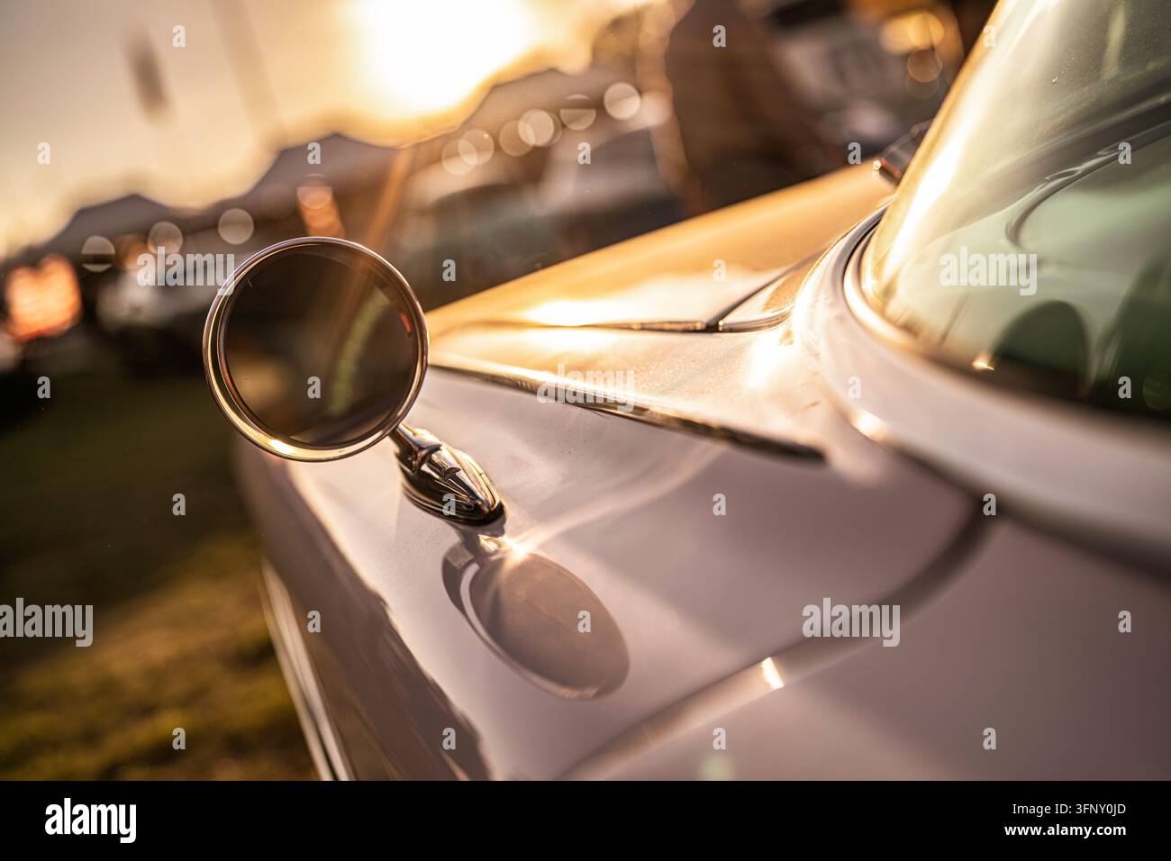 Specchietto laterale di auto vintage che riflette la calda luce dorata dell'ora blu, creando effetti di bokeh e sottolineando il design classico dell'automobile, evocando sentimenti di nostalgia Foto Stock