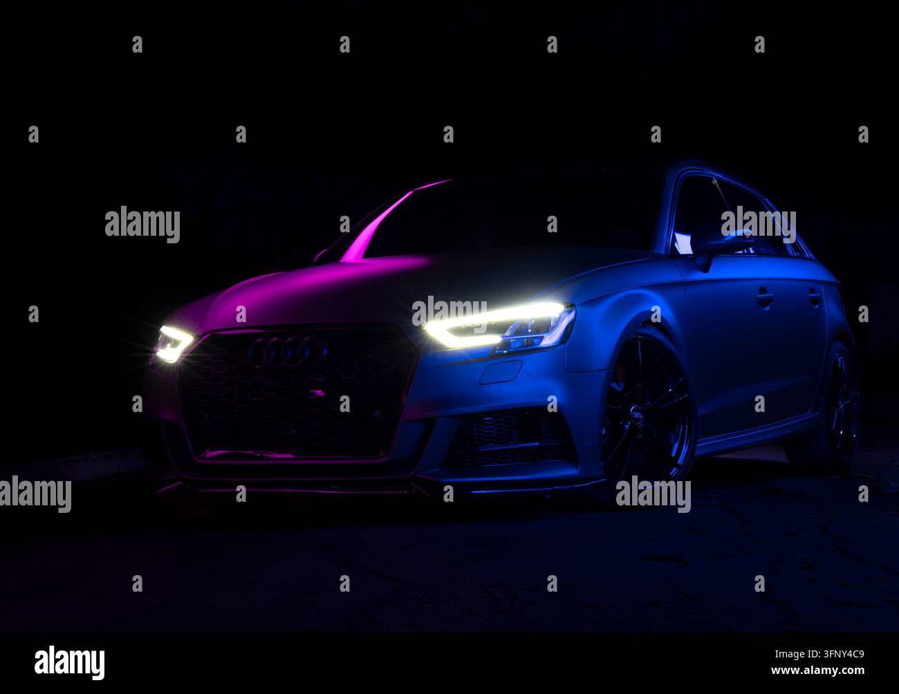 Autovettura hatchback di lusso che mostra un design elegante con illuminazione neon moderna viola e blu, evidenziando le prestazioni dinamiche e lo stile elegante del veicolo Foto Stock