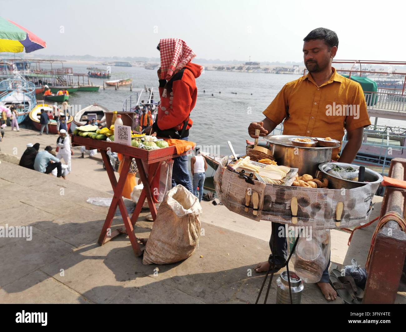 VARANASI, INDIA - 22 GENNAIO 2026: Venditori ambulanti di strada vendono snack accanto al Gange in un ghat affollato a Varanasi. Foto Stock