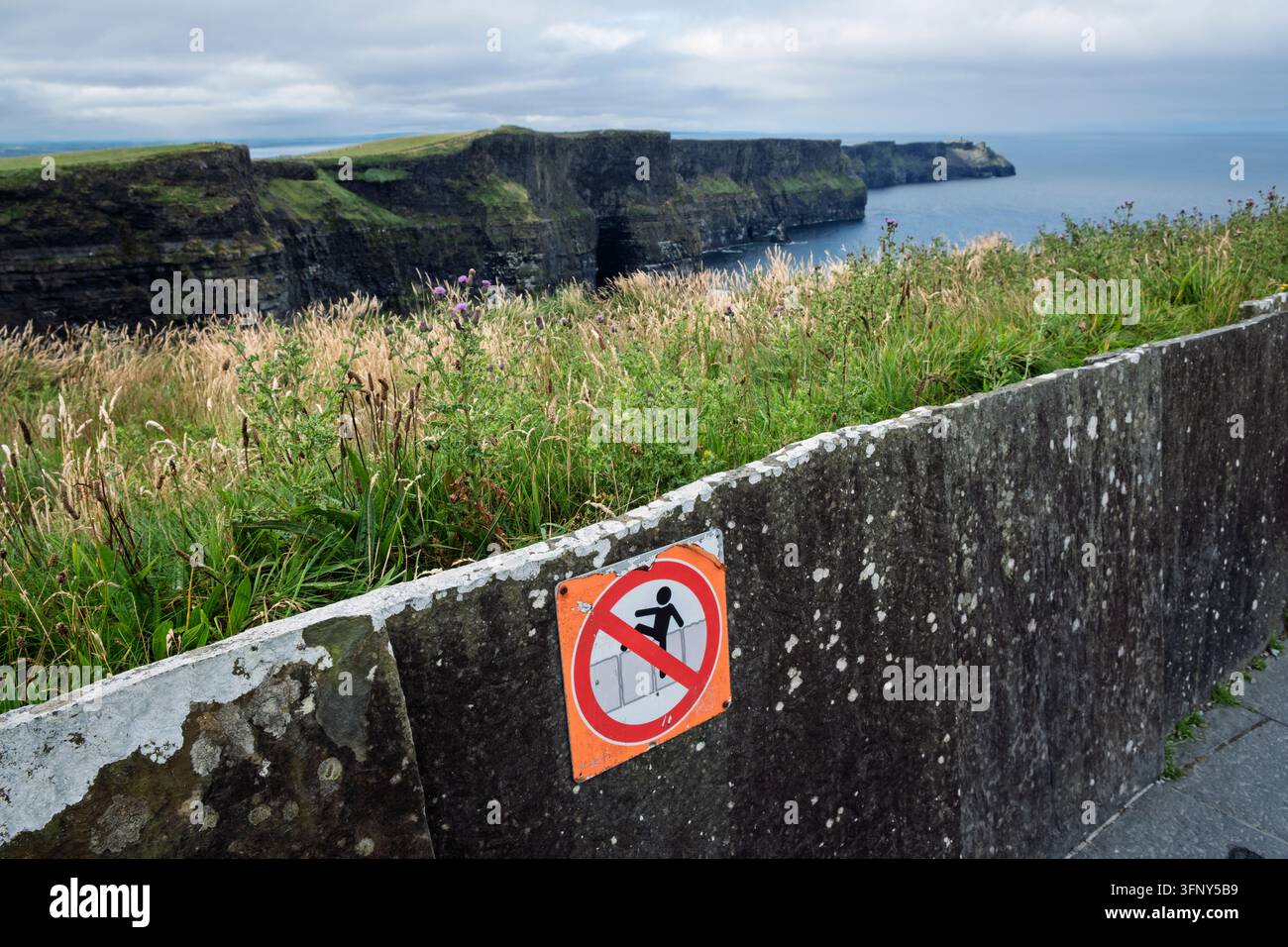 Segnale che avverte i visitatori di non arrampicarsi oltre il muro sul bordo della scogliera, Falesie di Moher, Contea di Clare, Irlanda Foto Stock
