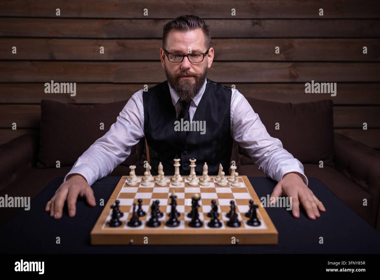 Un uomo serio seduto prima di una scacchiera Foto Stock