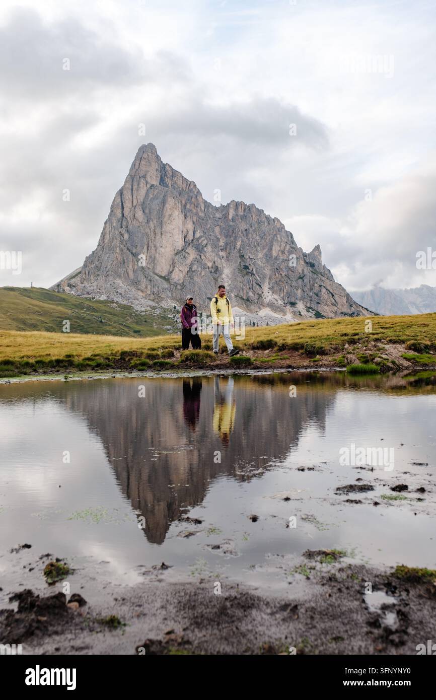 Due escursionisti vagano attraverso lo splendido scenario del Passo Giau nelle Dolomiti, Italia. I riflessi in uno stagno sereno esaltano il fascino pittoresco di Foto Stock