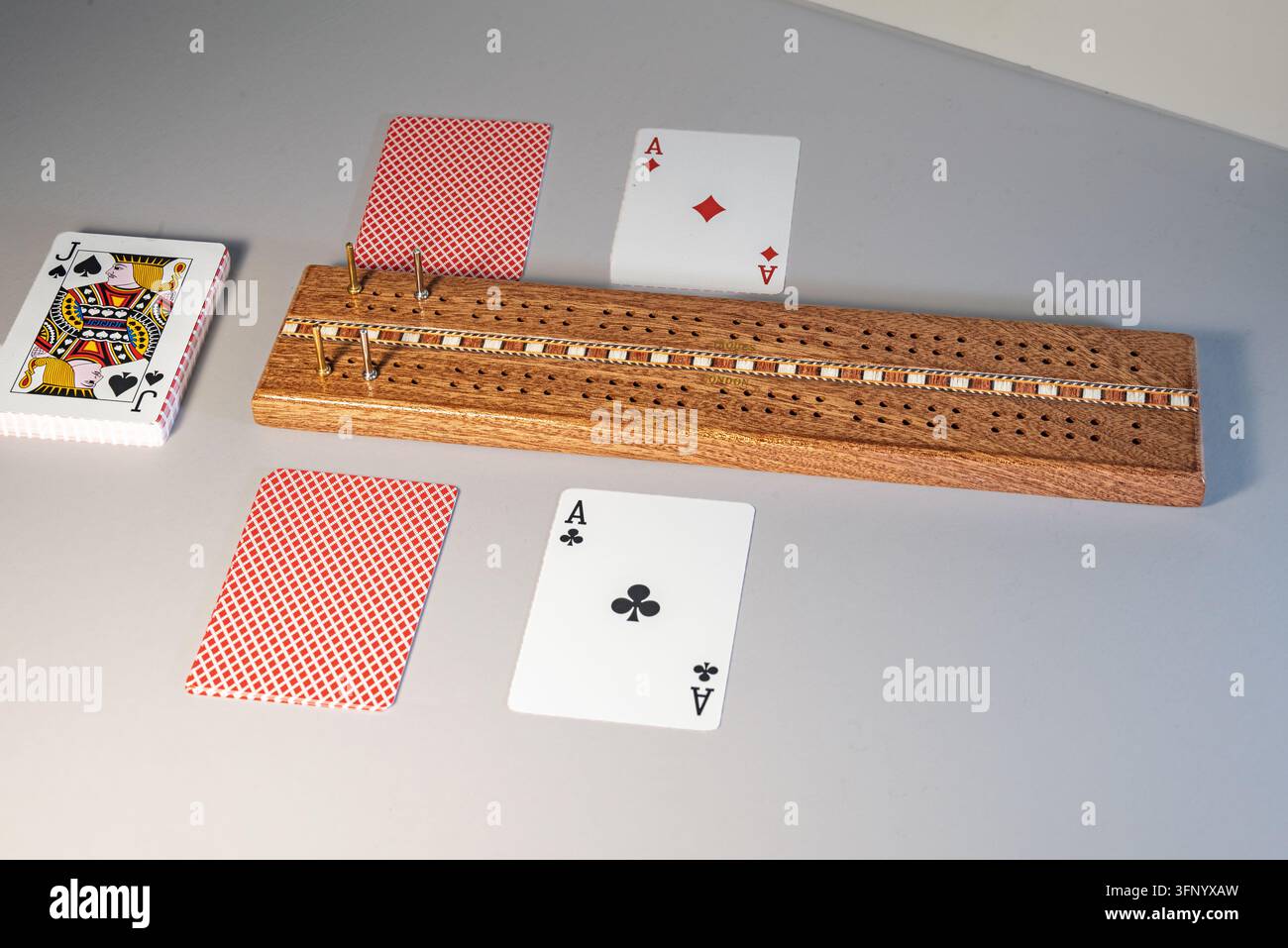 Tavola da cribbage in legno con pioli di metallo, un mazzo di carte, Asso di Quadri, Asso di Fiori e due carte coperte su una superficie grigia. Londra è visibile su Foto Stock