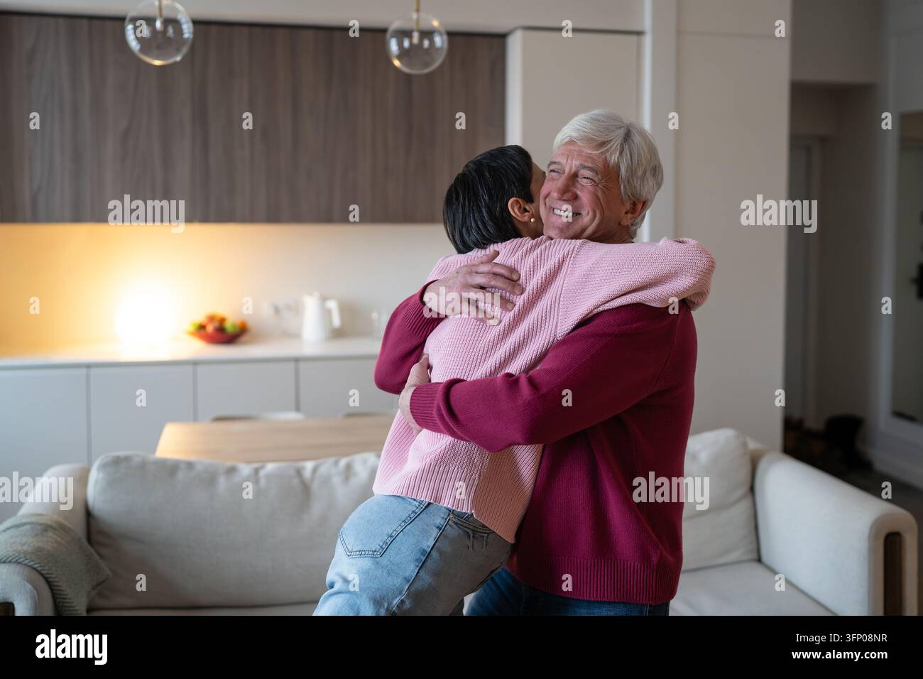 Marito anziano gioioso che sorride abbracciando la moglie affettuosa e positiva durante un momento familiare edificante. Foto Stock