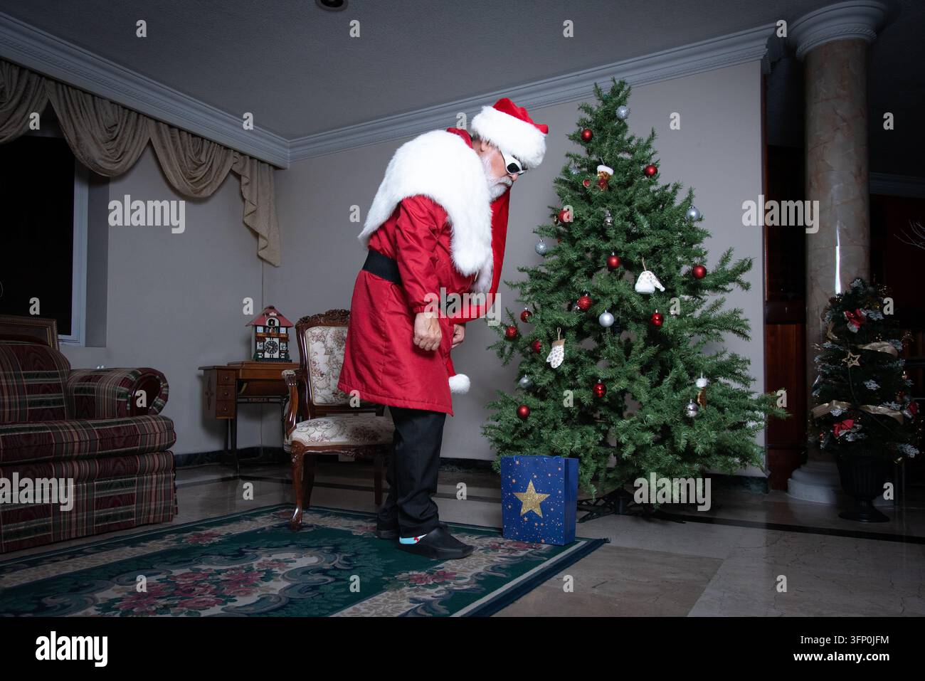 Babbo Natale che afferra una borsa regalo blu accanto all'albero di Natale Foto Stock