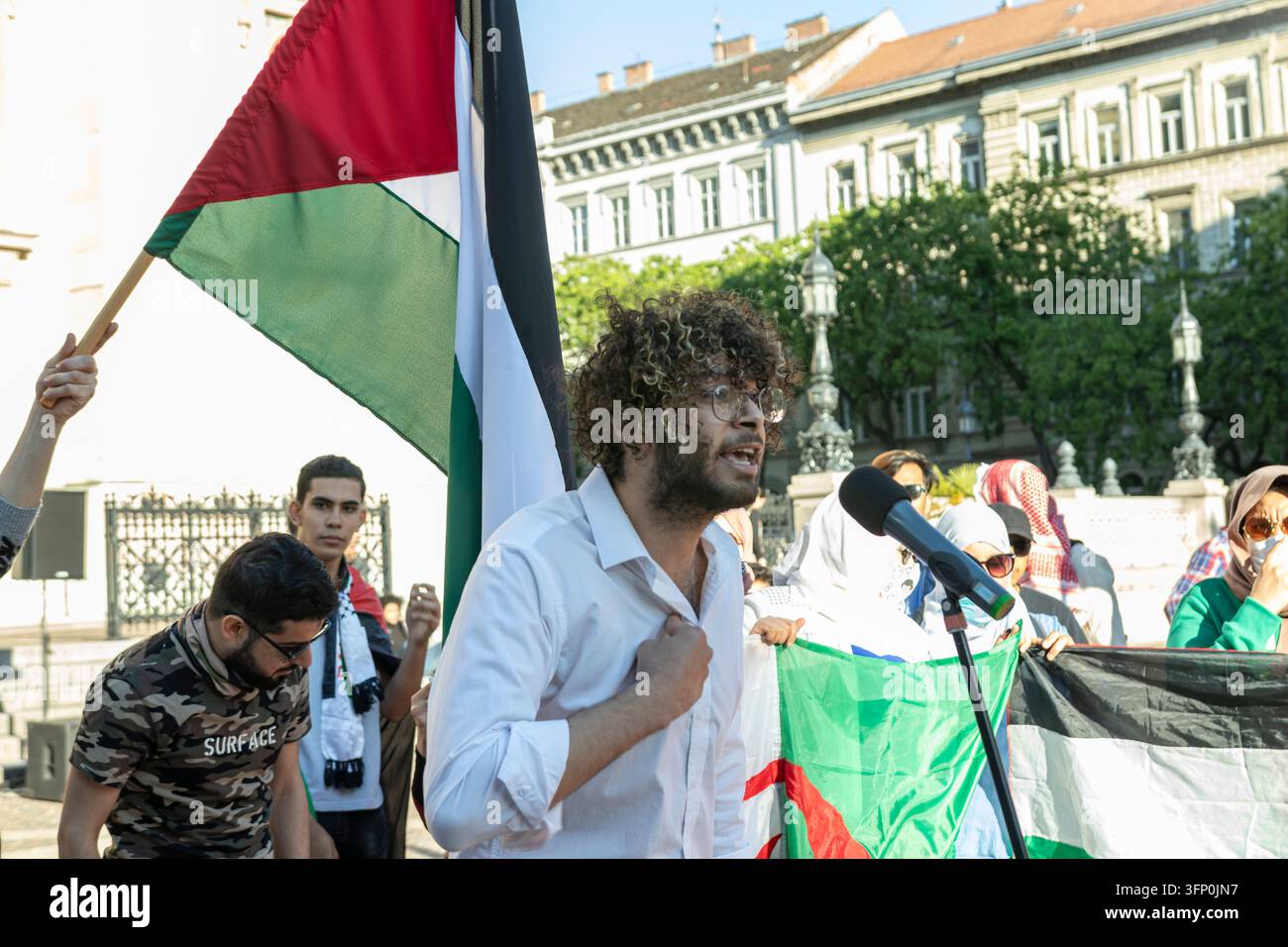 Ungheria, Budapest 2021 05 29: Un giovane dagli capelli ricci che parla in un microfono durante una manifestazione pro-Palestina, tenendo una bandiera palestinese, ou Foto Stock