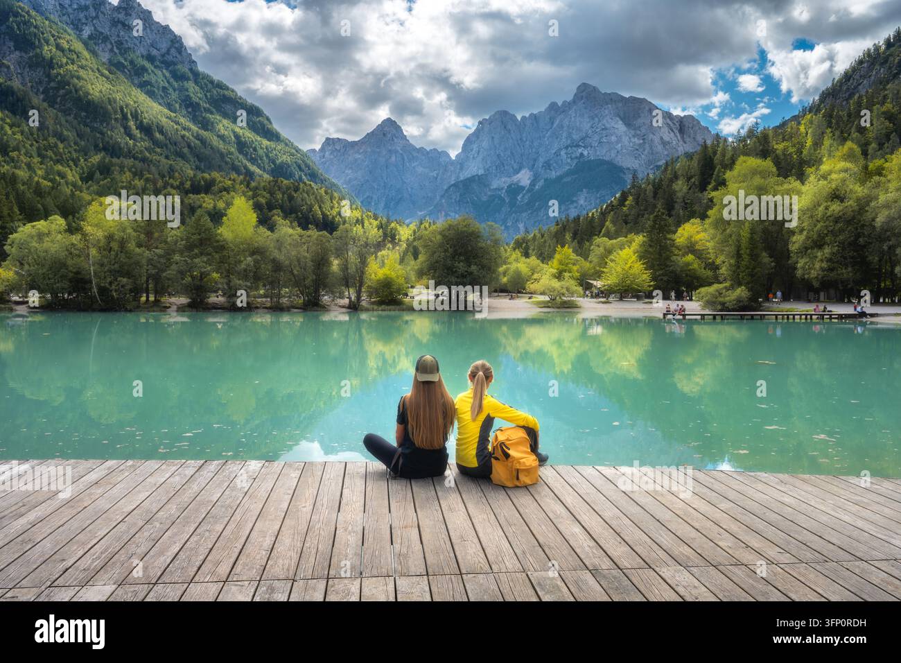 Due donne sedute su un molo di legno al lago Jasna in Slovenia Foto Stock