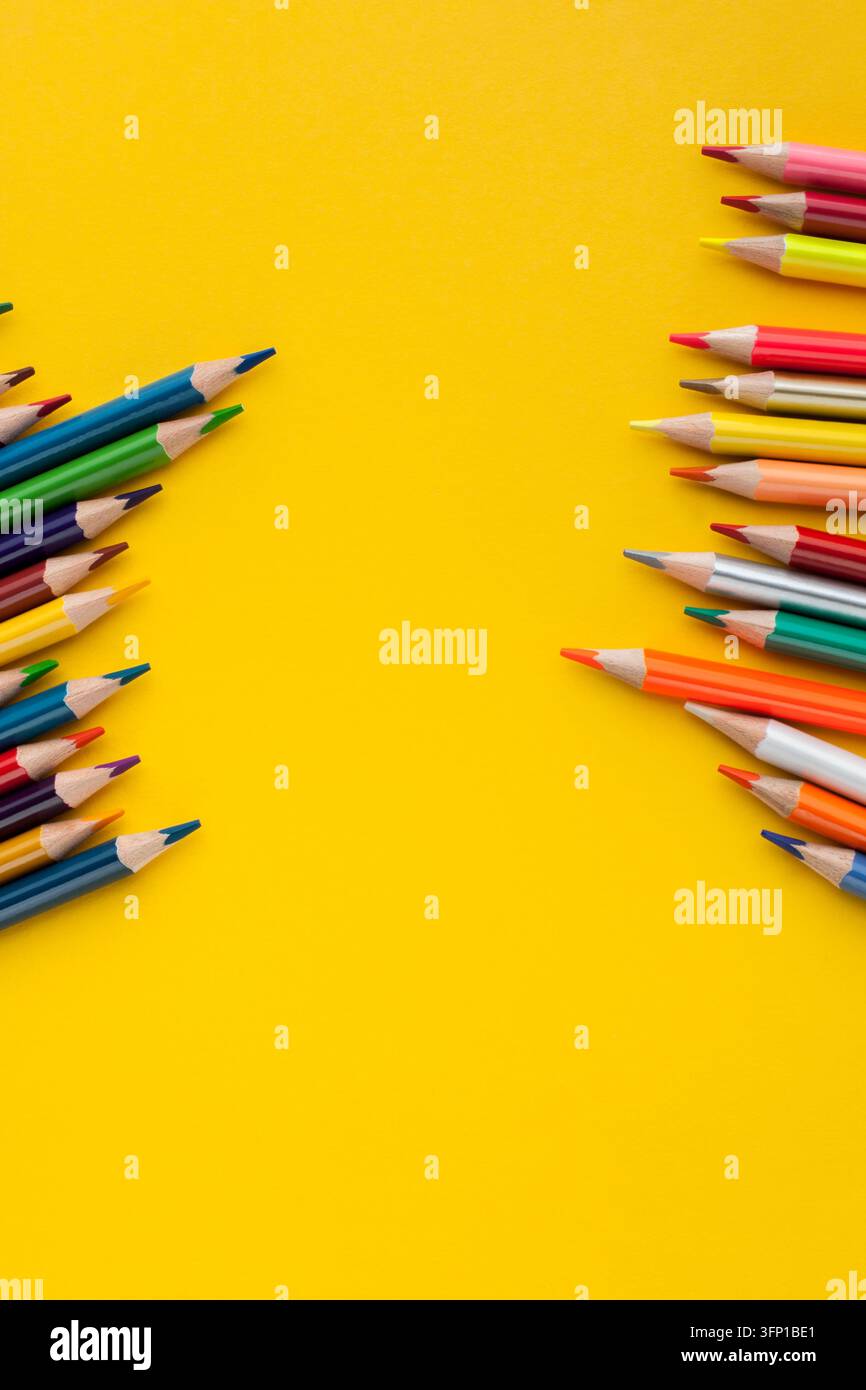 Pastelli colorati disposti su uno sfondo giallo brillante, creando una composizione vivace per l'arte, il disegno, la creatività, l'educazione e le forniture scolastiche Foto Stock