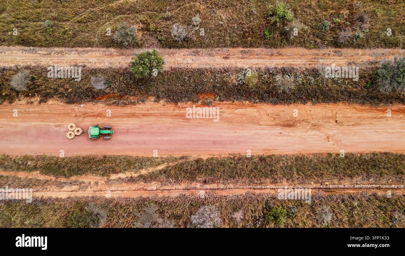 Vista aerea di un trattore verde che trascina pesanti pneumatici lungo una strada sterrata danneggiata per levigare e riparare la superficie nel paesaggio rurale di Stellenbosch Foto Stock