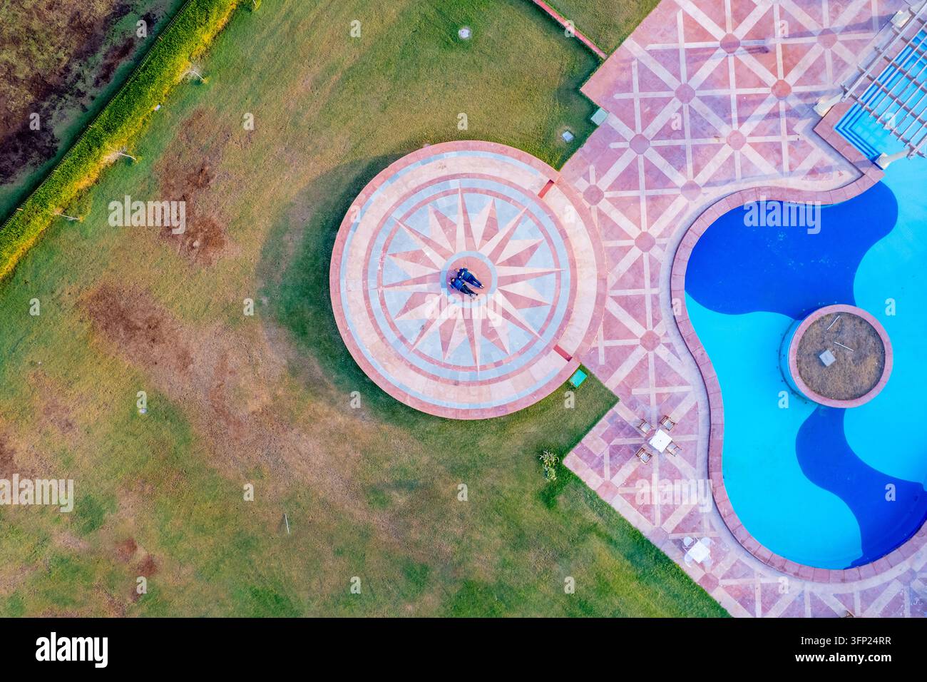 Vista aerea di un resort elegante con una piscina e un terrazzo circolare con lavorazione in pietra tradizionale Rajasthani, con due persone sul P geometrico Foto Stock