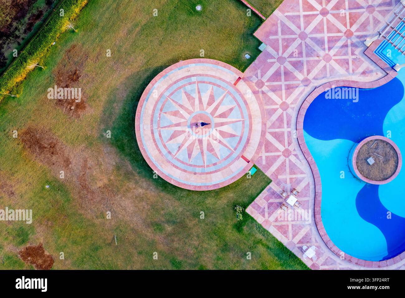 Vista aerea di un elegante resort con un terrazzo circolare in pietra con motivi tradizionali del Rajasthan, una piscina blu e prati verdi ben curati Foto Stock