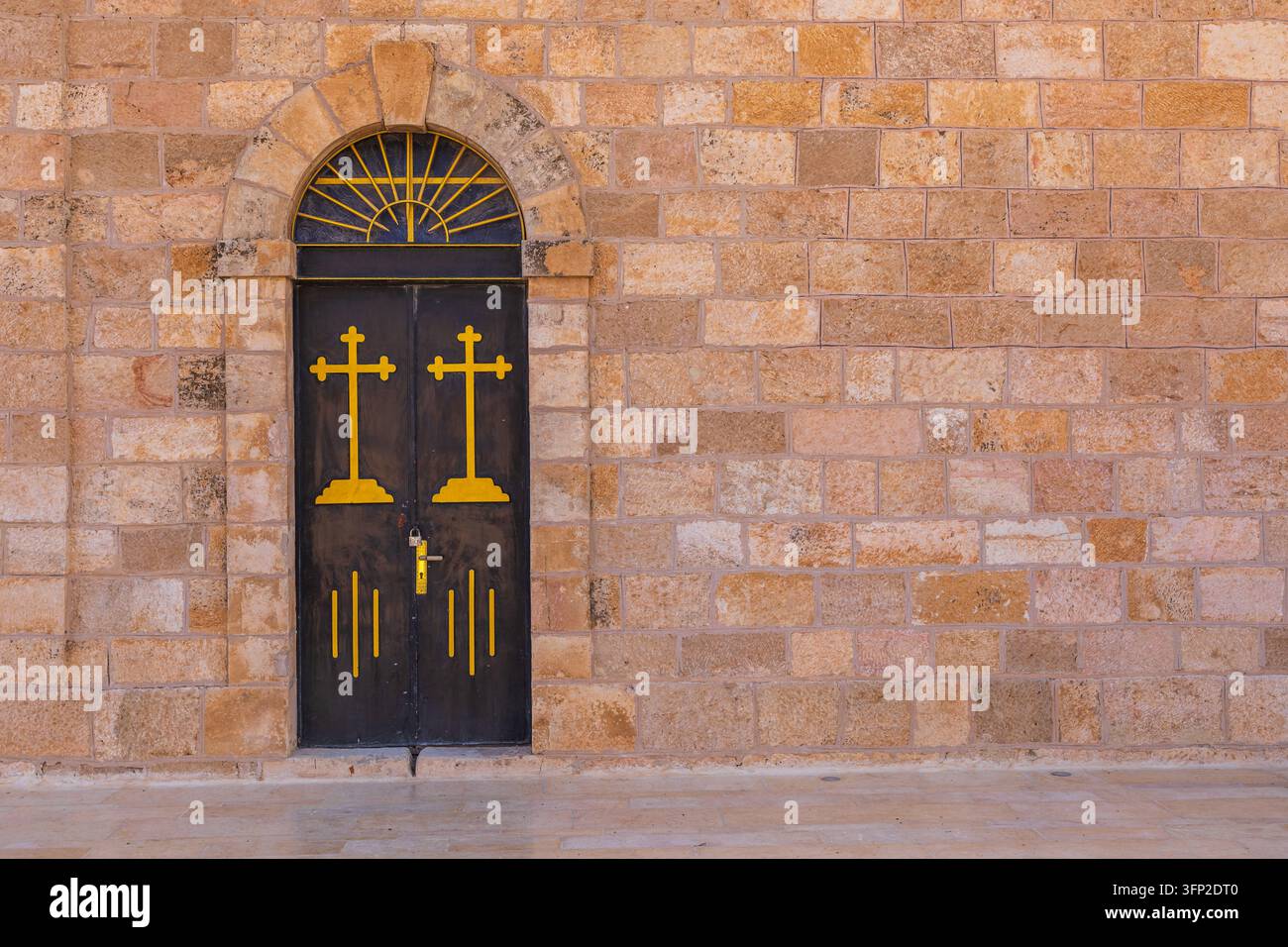 Vista di una porta di legno scuro adornata con croci gialle e una finestra semicircolare inserita in un muro di pietra chiaro strutturato a Madaba, governatorato di Madaba Foto Stock