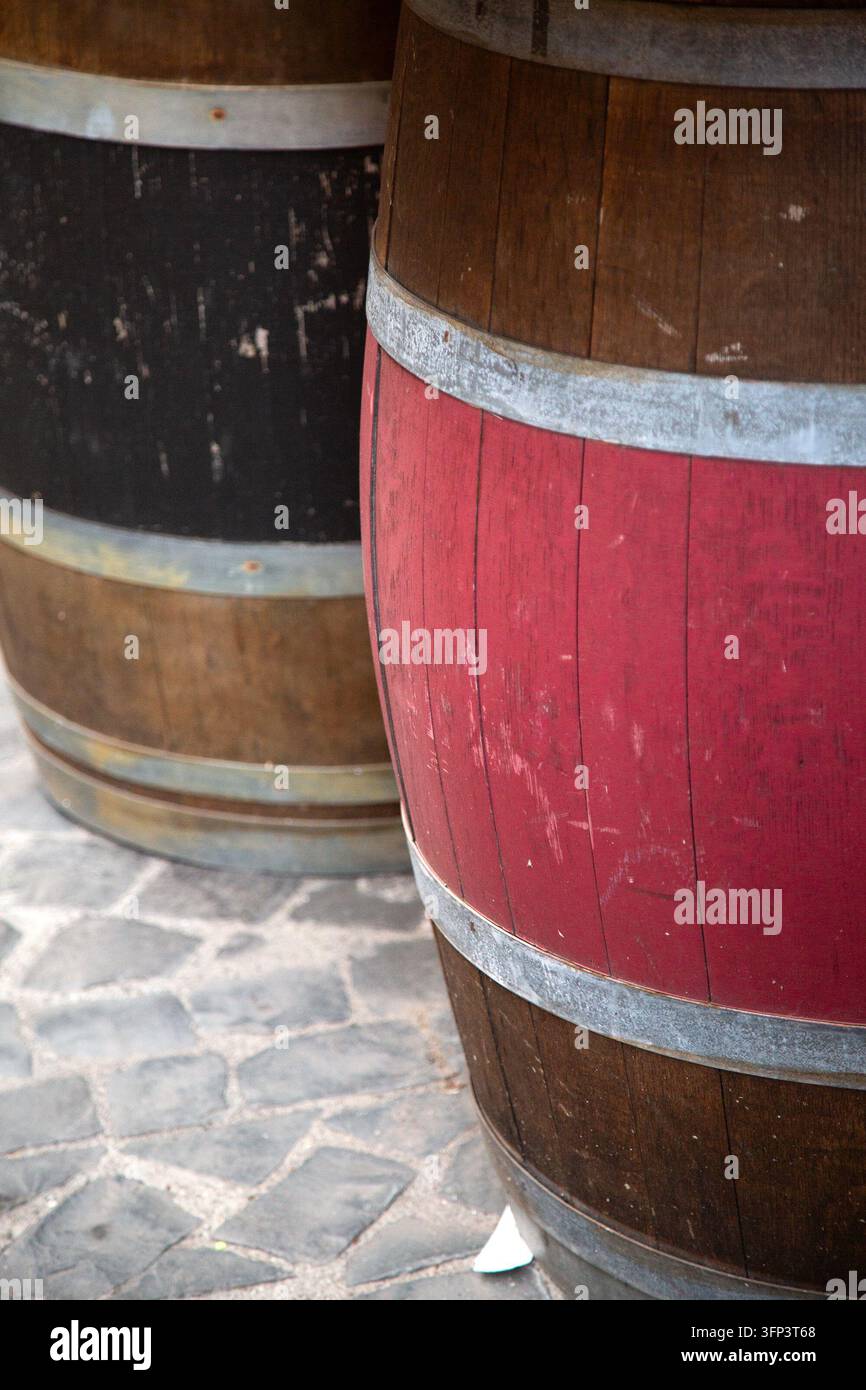 Barili di legno stagionati con doghe dipinte di rosso e cerchi metallici su pavimentazione in pietra, che mostrano una texture rustica, superfici invecchiate e tagliate da vicino Foto Stock