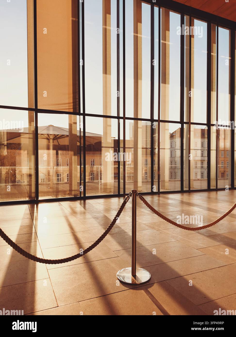 Calda luce dorata della sera che filtra attraverso grandi finestre di vetro in una sala museale contemporanea minimalista con una corda di barriera. Foto Stock
