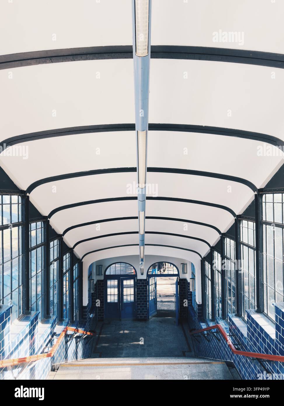 Vista simmetrica ad angolo alto delle scale per passeggeri che conducono alle porte blu della storica stazione S-Bahn di Heerstraße. Foto Stock