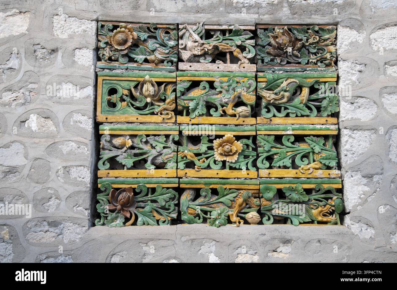 Un pannello decorativo di piastrelle di ceramica smaltate verdi e gialle con motivi floreali a volute e uccelli, inserito in un muro di pietra a Handan, Hebei, Cina Foto Stock