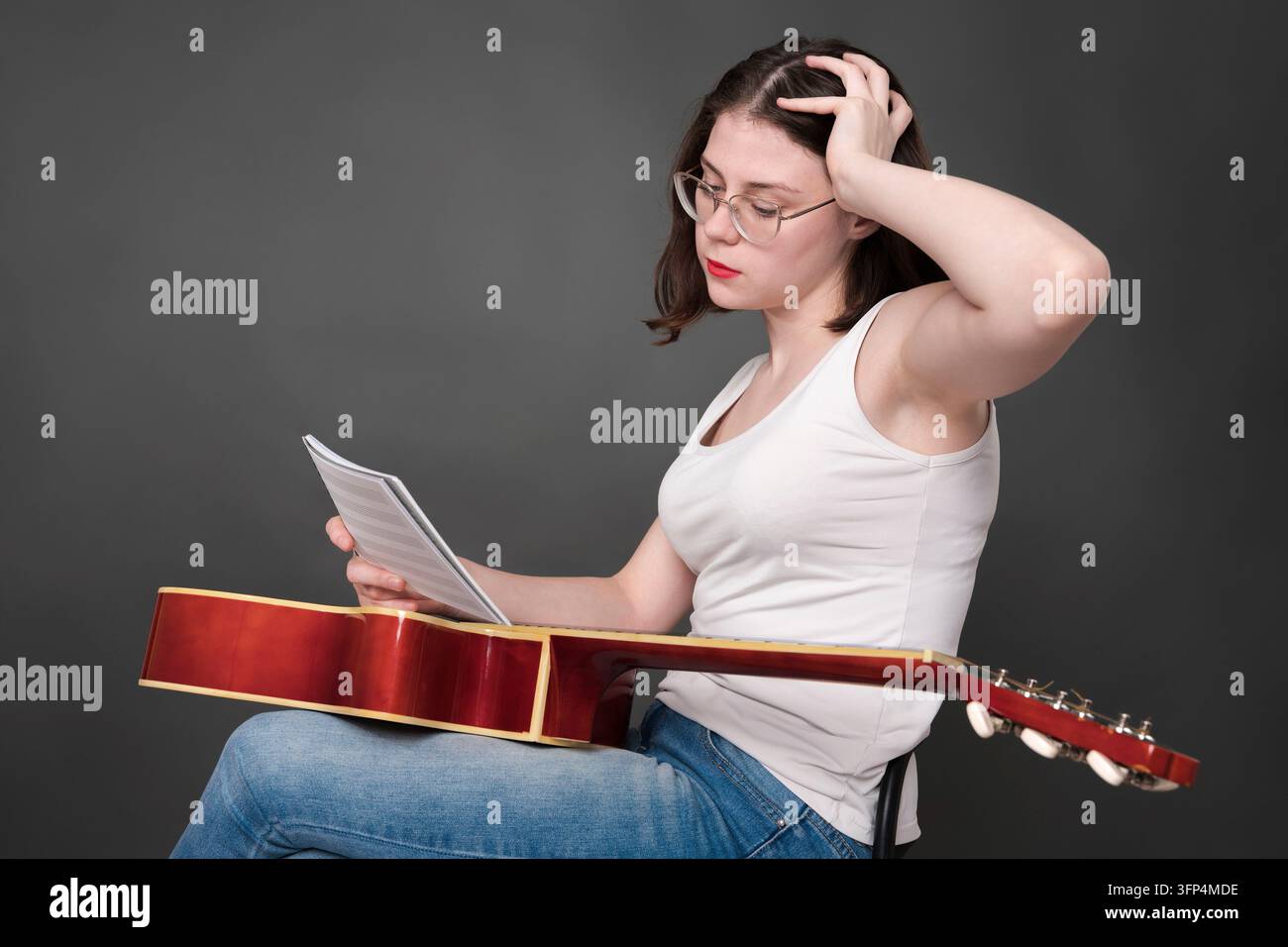 La musicista femminile perplessa tiene di fronte a lei note musicali, decifrando e analizzando la nuova creazione musicale. Cantautrice donna seduta con g Foto Stock