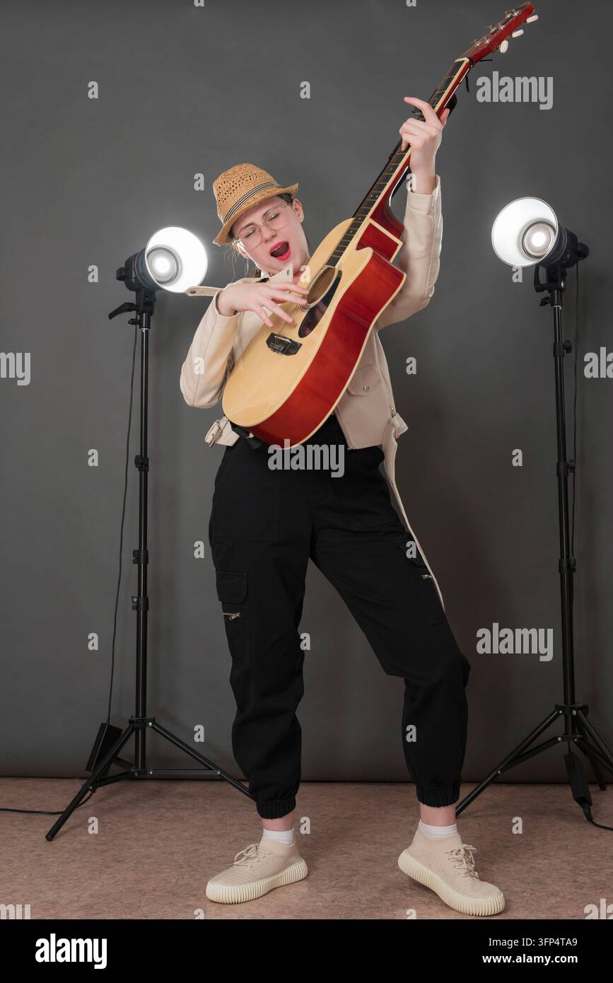 Cantante e chitarrista espressiva che suona la chitarra classica cantando una canzone con gli occhi chiusi, in piedi a figura intera sul palco Musicista giocosa Foto Stock