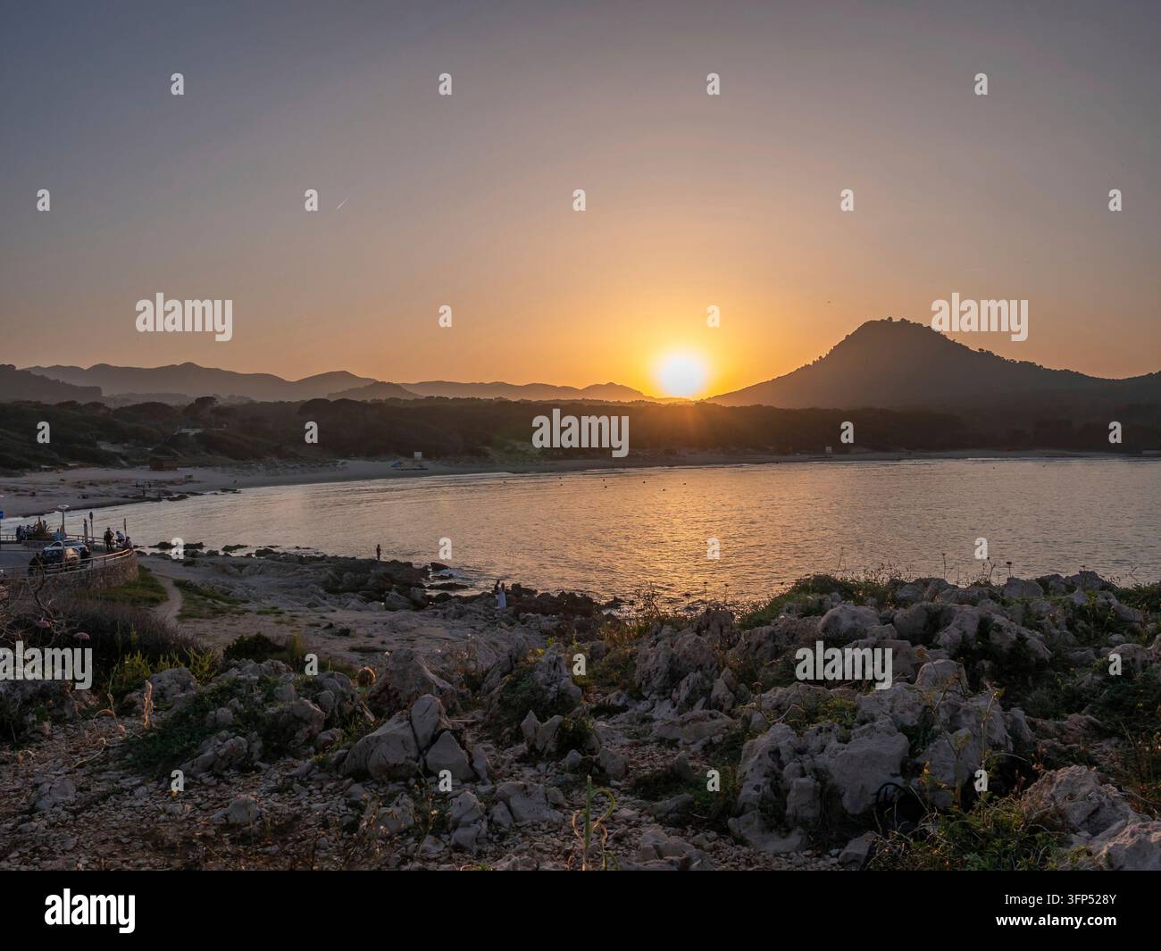 Un tramonto sereno a Cala Rajada, un calmo specchio d'acqua di Maiorca con una montagna lontana e una costa rocciosa, bagnata dalla calda luce dorata, Cala Ratjada, ma Foto Stock