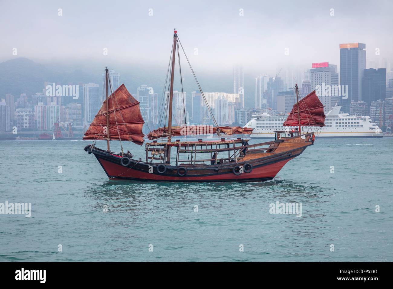 Il lungomare nebbioso di Hong Kong e una nave da crociera moderna. Una giunca tradizionale con vele rosse Foto Stock