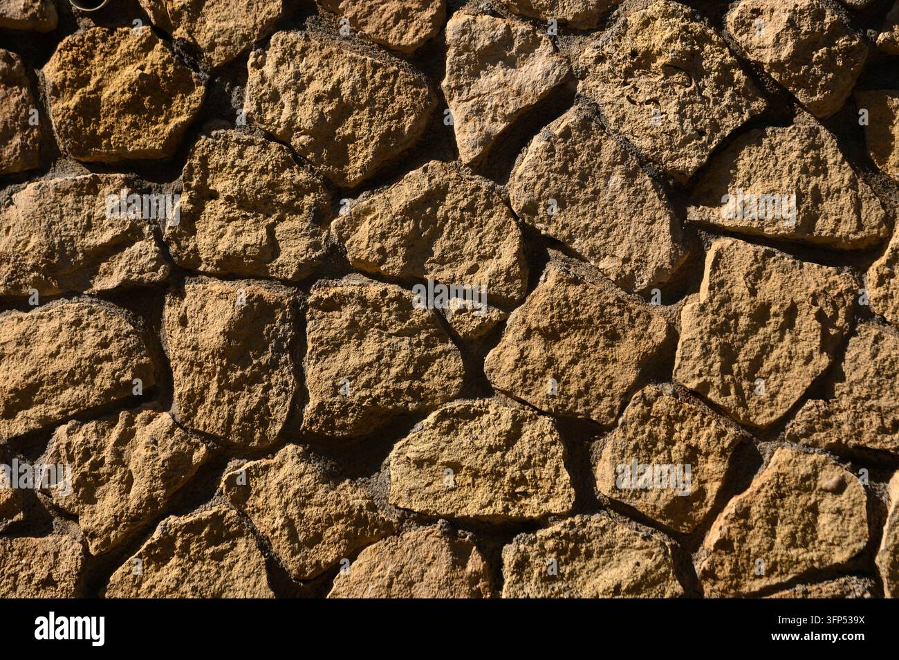 Un solido muro di pietra mostra una disposizione armoniosa di rocce irregolari, catturando l'essenza dell'arte della natura. La luce del sole danza sulla superficie Foto Stock