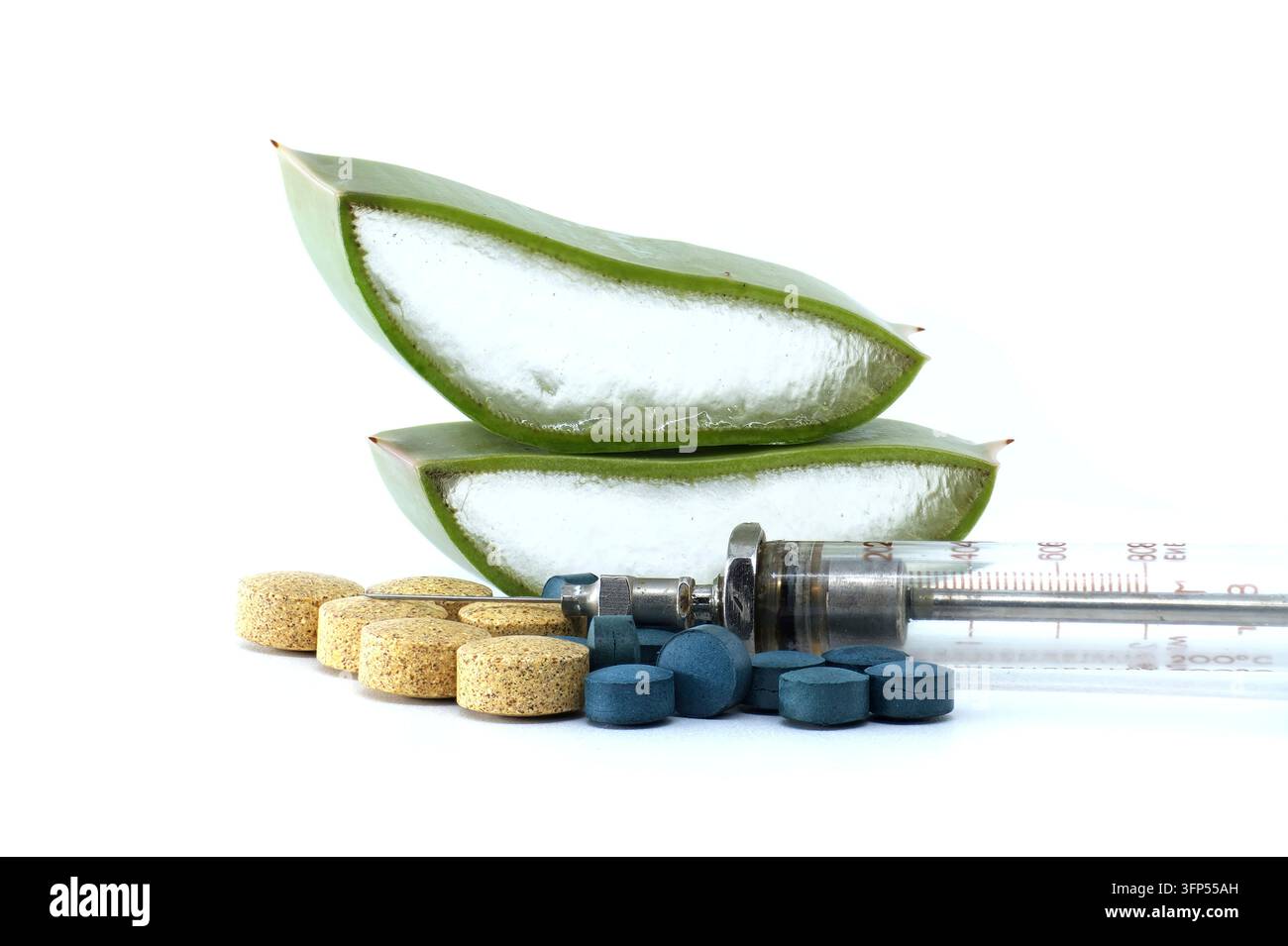 Primo piano di fette fresche di aloe vera accanto a una collezione di pillole blu e gialle e a una siringa medica antica Foto Stock
