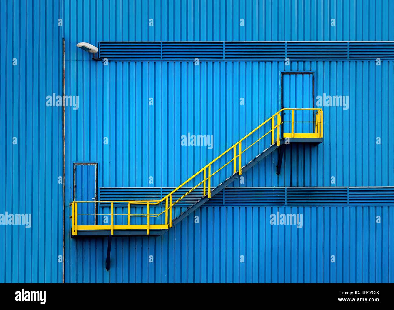 Facciata lineare blu con una scala gialla che separa un ingresso e un'uscita, presentando elementi quotidiani. Foto Stock