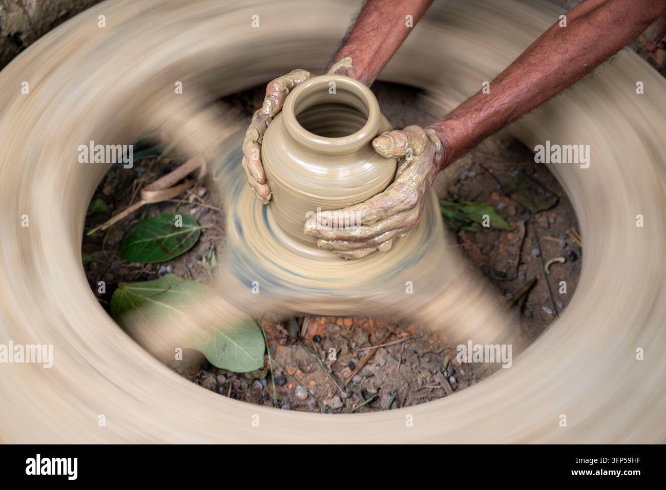 Joypurhat, division di Rajshahi, Bangladesh – 23 settembre 2026: Vista di un vasaio che modella un vaso di argilla su una ruota girevole con le mani coperte di argilla bagnata. Foto Stock