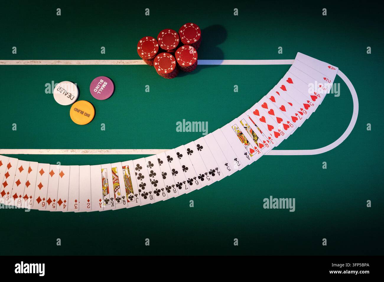 Ampio giocatore di carte si estende su un tavolo da poker in feltro verde. Un gruppo di gettoni rossi è posizionato accanto al bottone del dealer e ai dischi dei bui colorati. Foto Stock