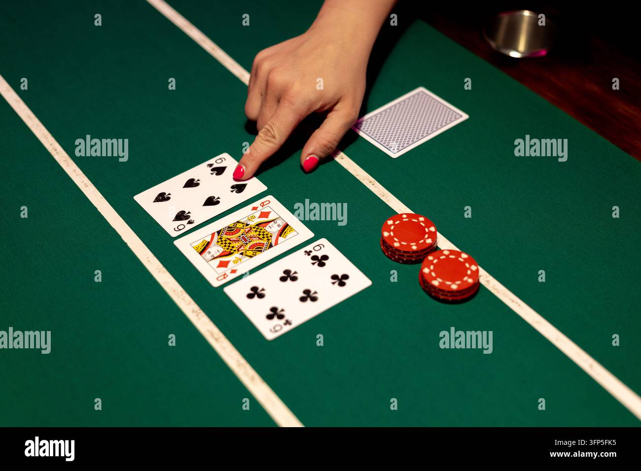 La mano di una dealer donna tocca il sei di picche su un tavolo da poker verde. La disposizione rivela tre carte comuni aperte, inclusa la regina di quadri. Foto Stock