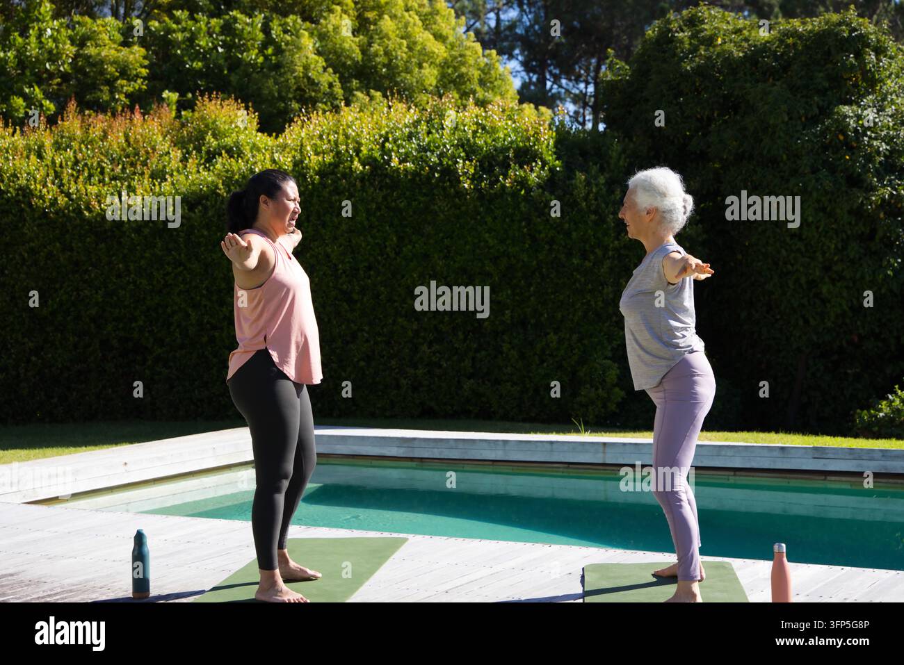Diverse amiche che praticano pose di equilibrio su materassini verdi in piscina nel cortile con due bottiglie Foto Stock