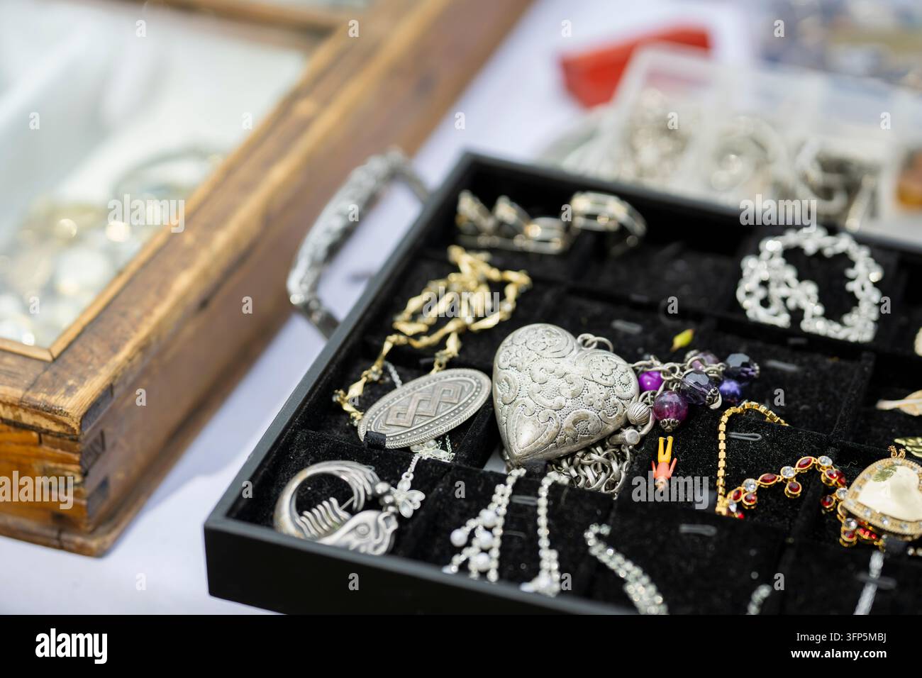 Gioielli vintage disposti in un vassoio nero, con ciondoli argentati ornati, ciondoli a forma di cuore, collane di perle e braccialetti. Foto Stock