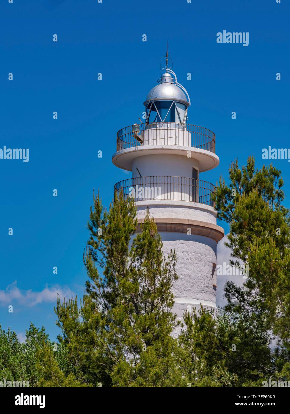 Torre cilindrica bianca di faro si erge contro il brillante cielo blu mediterraneo a Port de Soller, incorniciata da lussureggianti pini verdi - costa classica Foto Stock