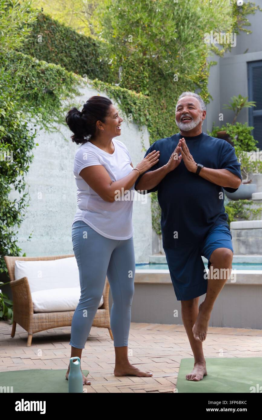 Coppia afroamericana che pratica yoga su una terrazza piastrellata vicino alla piscina su materassini verdi, indossa abbigliamento sportivo Foto Stock
