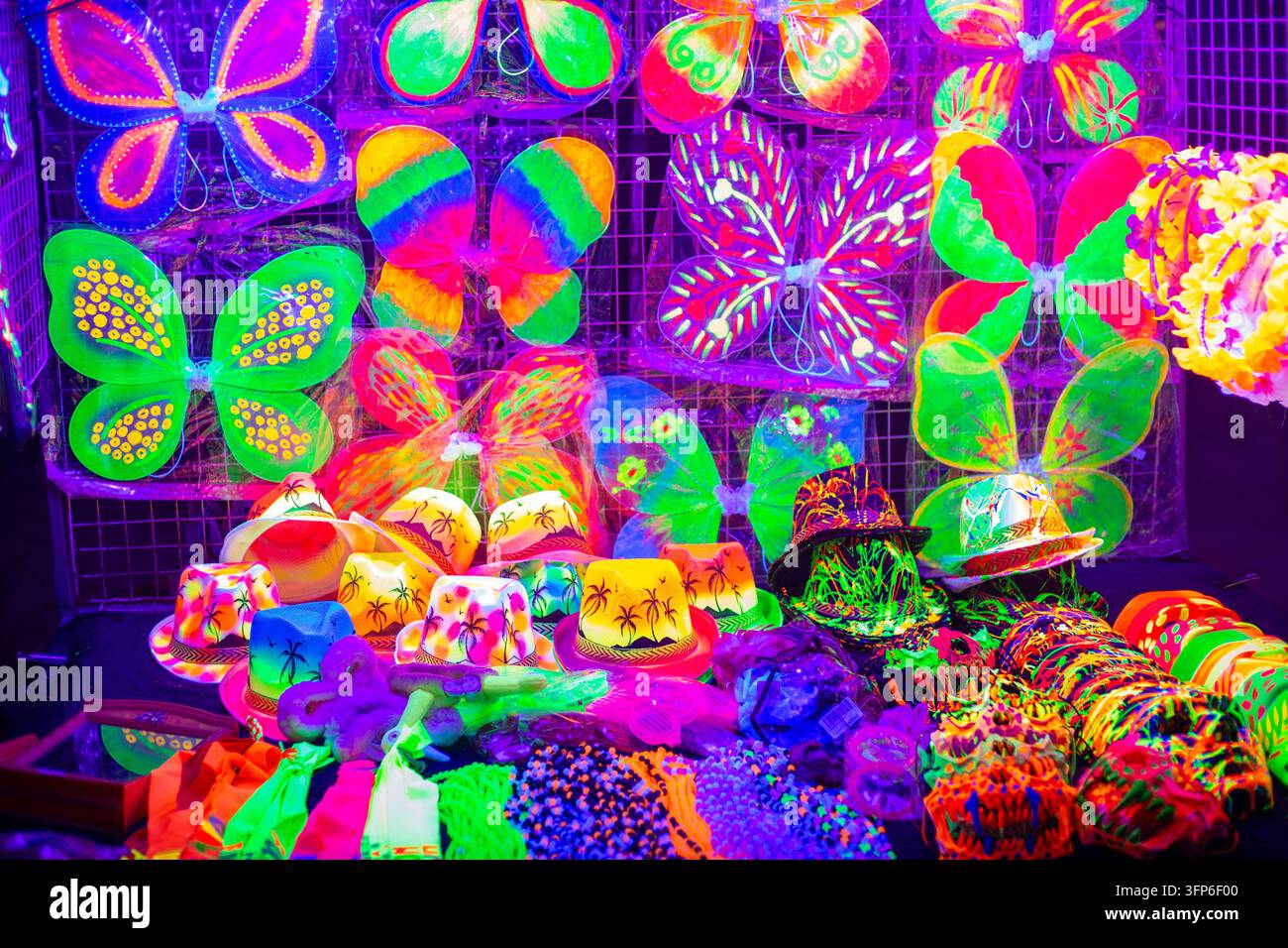 Ali neon colorate luminose e cappelli da festa sono esposti su uno stand del mercato notturno. Souvenir per la festa della luna piena, shopping, accessorio per festival sulla spiaggia tropicale Foto Stock