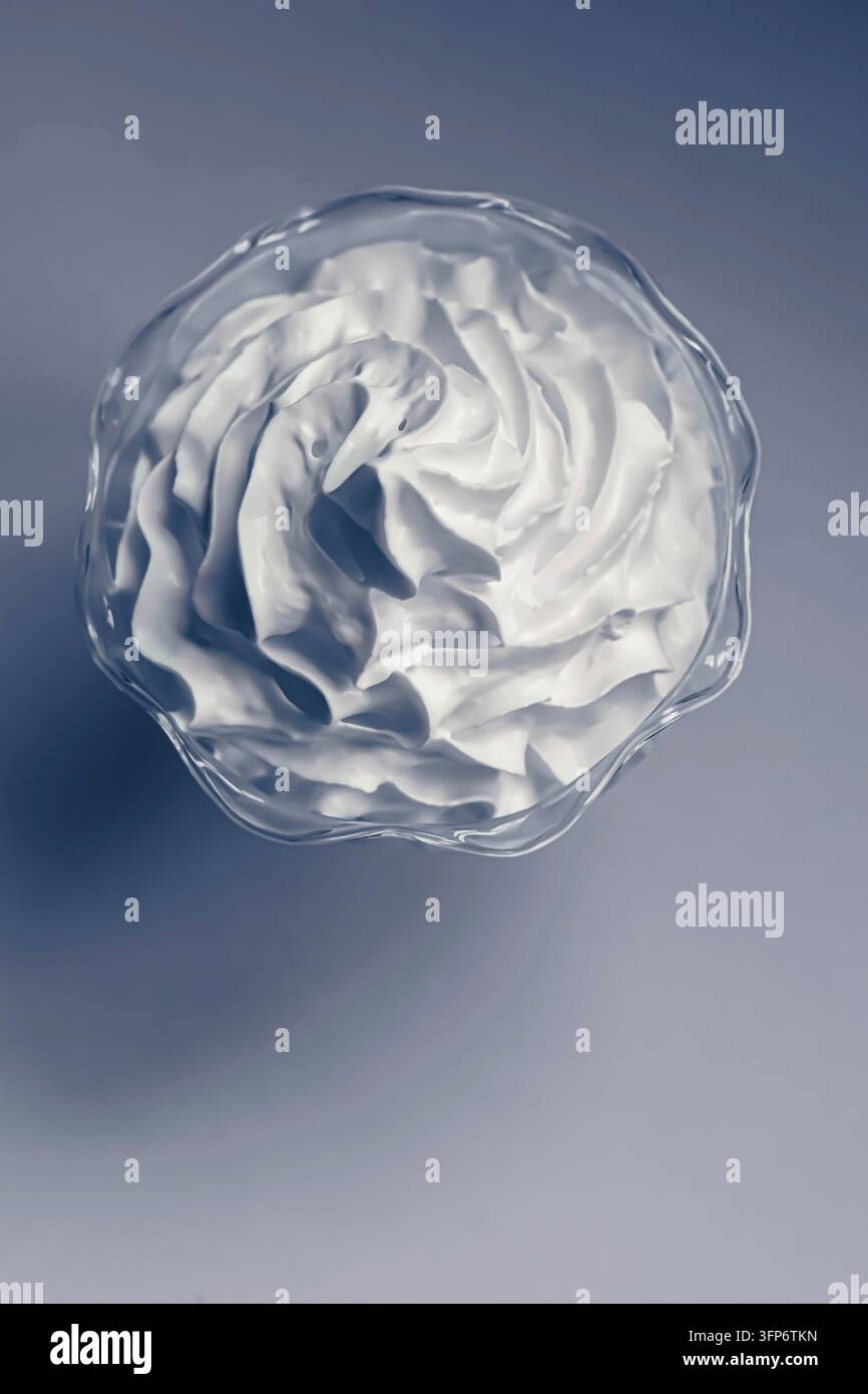 Panna montata che forma un vortice decorativo in una ciotola di vetro trasparente, mostrando una consistenza cremosa, morbidezza e dolce indulgenza Foto Stock