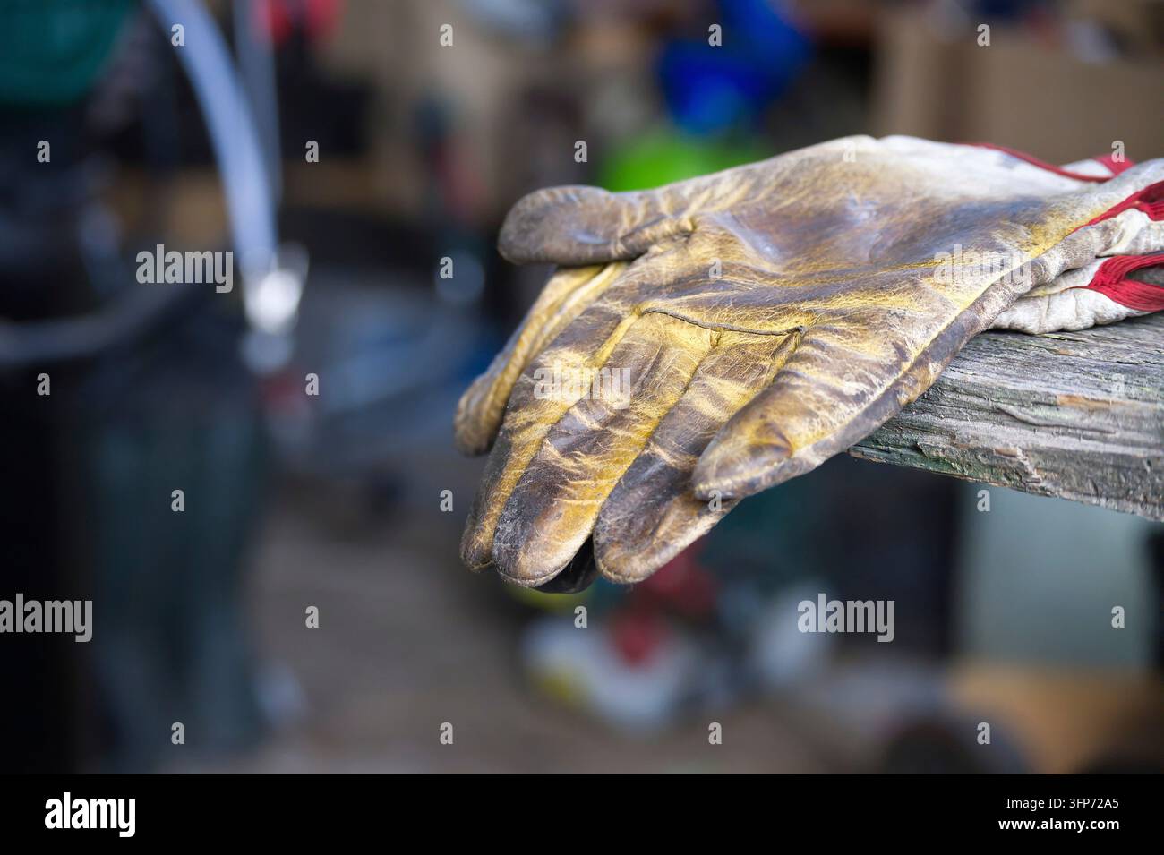 Un paio di guanti da lavoro in pelle fangosa si avvolge su una panca ruvida e resistente alle intemperie in un'officina vivace. La consistenza usurata e la sporcizia conferiscono un duro lavoro manuale Foto Stock